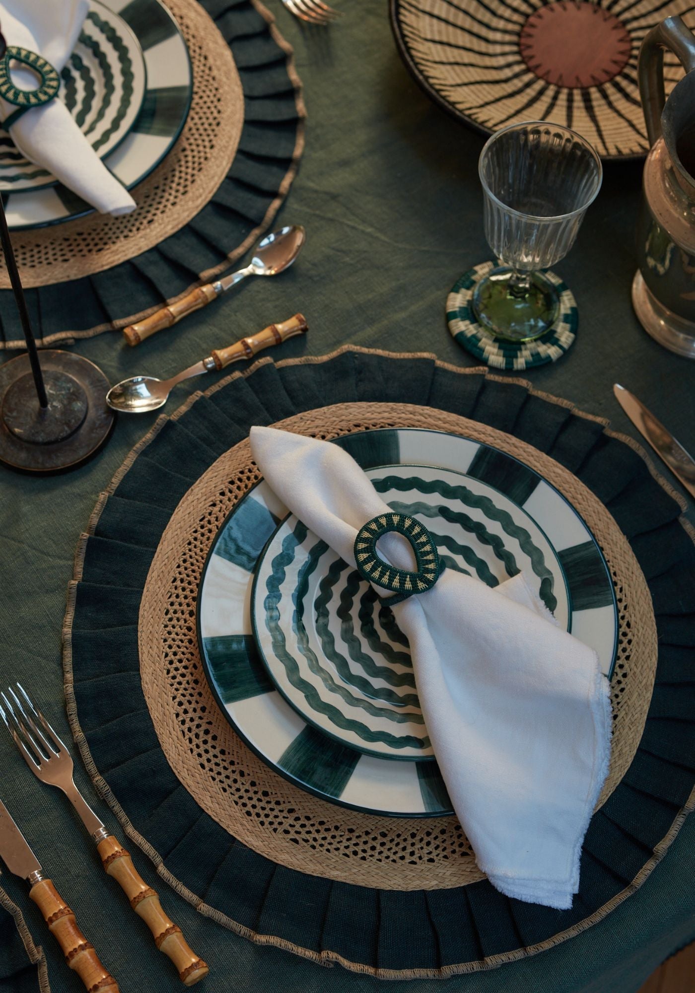 Sunset Musings tablescape featuring teal geometric hand-painted plates, woven placemats with linen ruffles, and teal werregue accessories styled with bamboo cutlery.