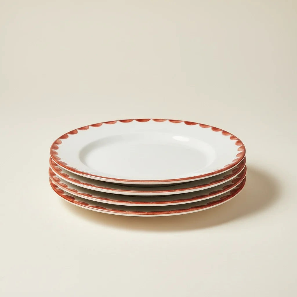 Stack of white plates with scalloped red rim on a beige background