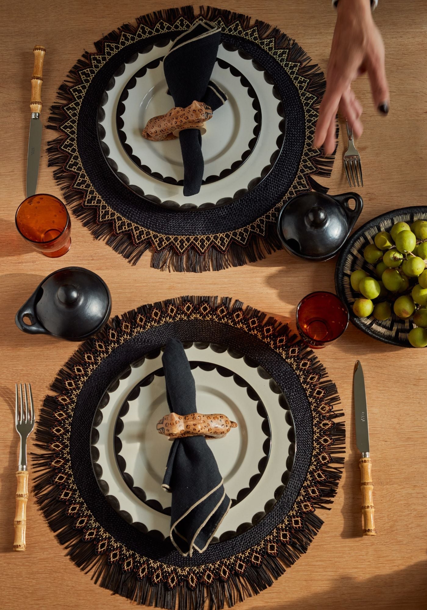 Lunch Time Rumba tablescape featuring black and gold beaded placemats, ivory and black scalloped plates, Felino napkin rings, and bamboo cutlery with black pottery accents.