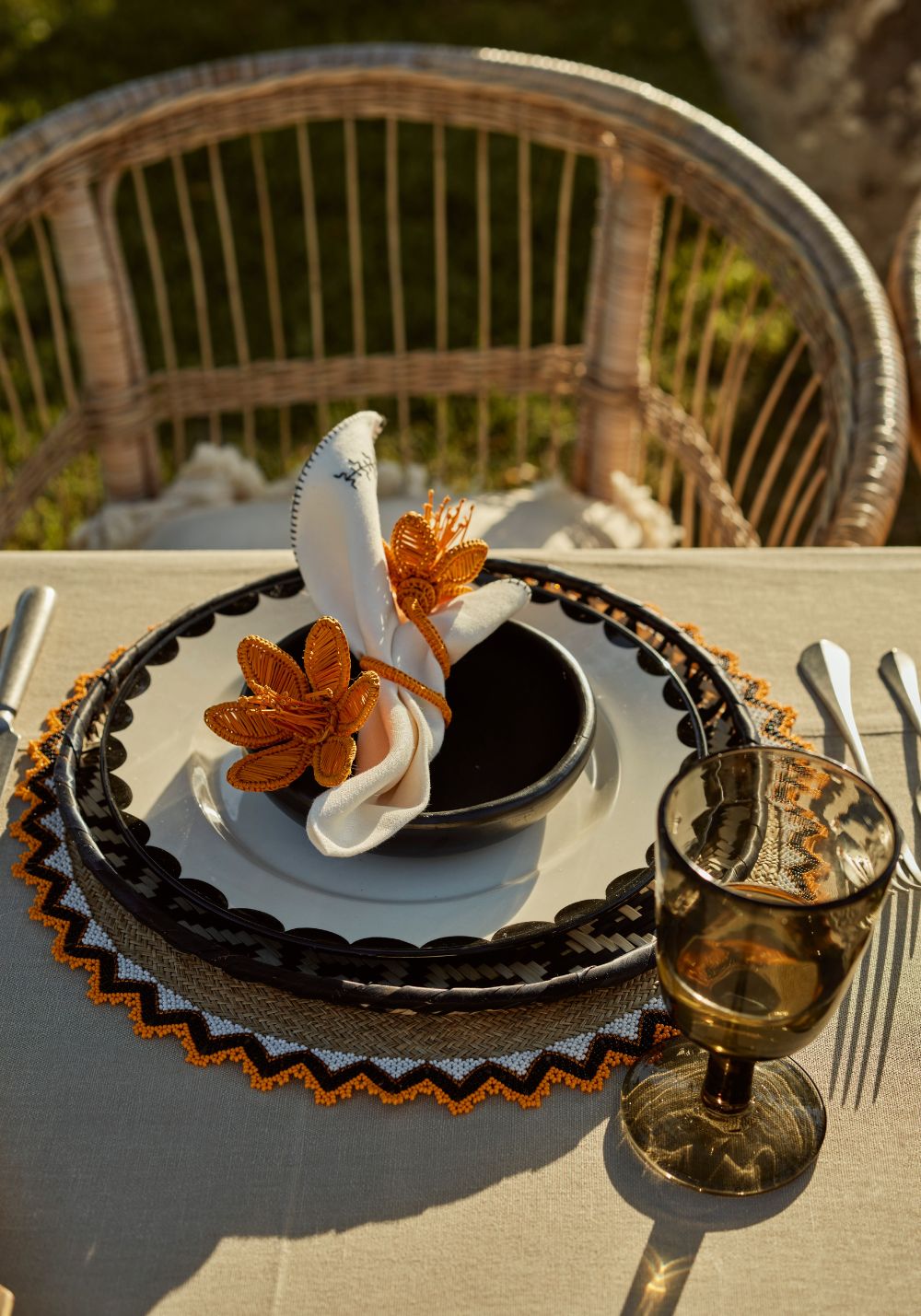 Summer Love tablescape featuring black and ivory ceramics, orange and black beaded placemats, and bright orange beaded flower napkin rings styled for an outdoor summer setting.